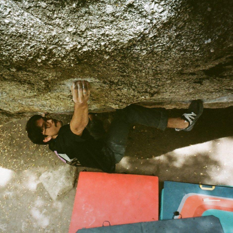  Looking down at  MHW Athlete Noah Wheeler with chalky hands, bouldering in a relaxed-fit tee above crash pads.


