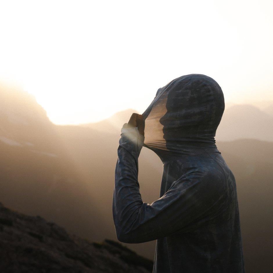 A man stretches the hood of his Crater Lake™ Long Sleeve Hoody. His profile silhouette is seen as light shines through the fabric.



