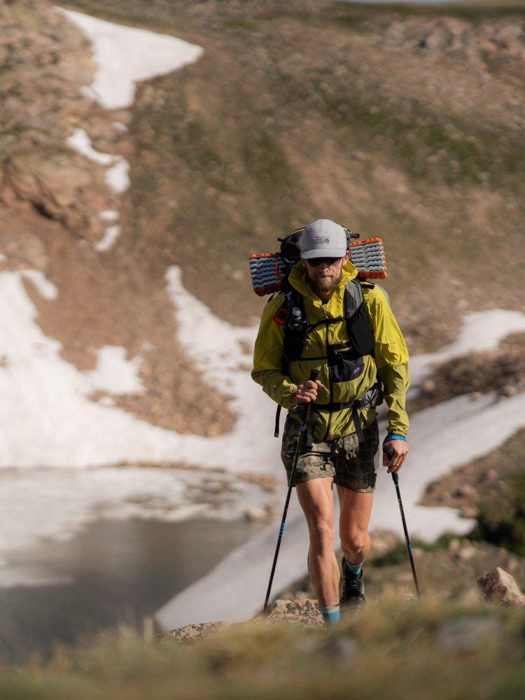  A man with a loaded pack and hiking poles wearing a Wind Veil™ Hooded Jacket ascends out of the valley.


