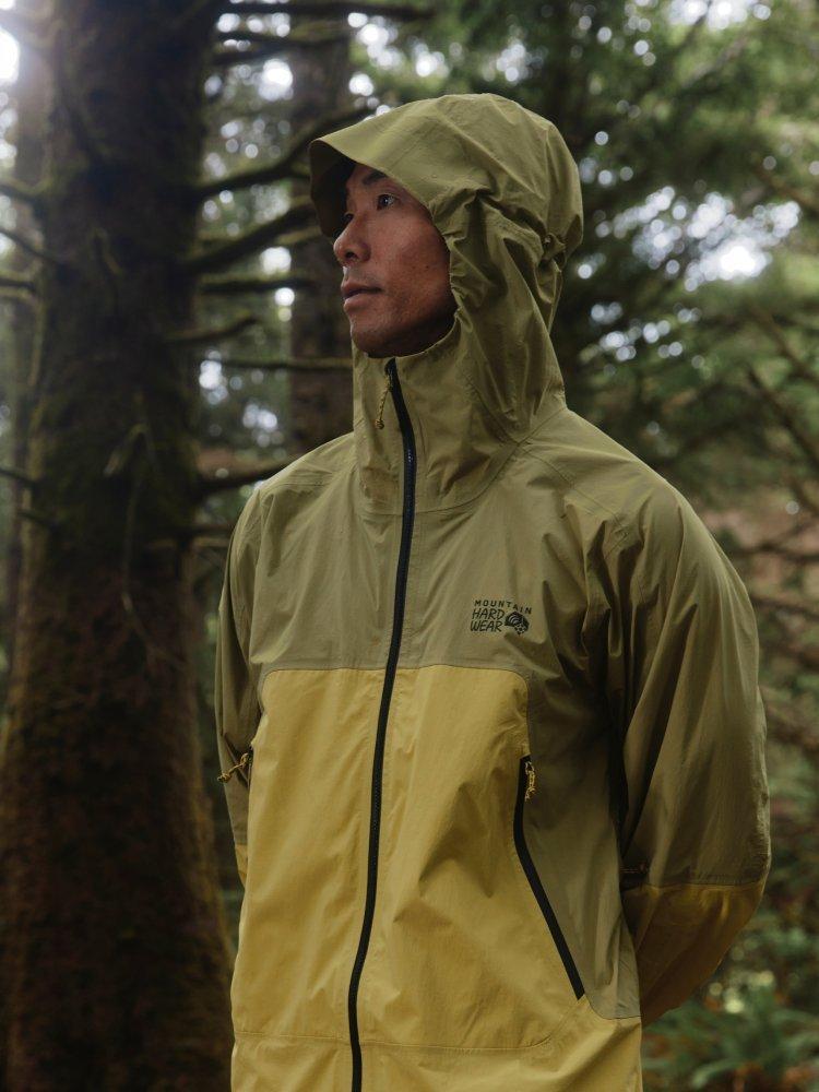 A man stands in a rainy forest wearing a Cloud Cipher™ Hooded Jacket, zipped with the hood up.


