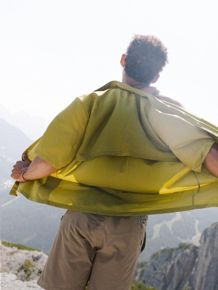 Facing away, at the summit, a man removes his button-down Sun Drift™ Cooling Short Sleeve Shirt.


