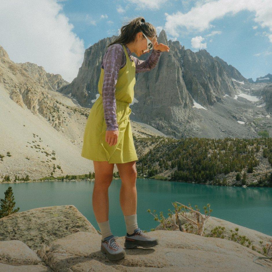 Woman wearing hiking boots with a Dynama™ Dress and Crater Lake Long Sleeve Shirt peers over ledge.