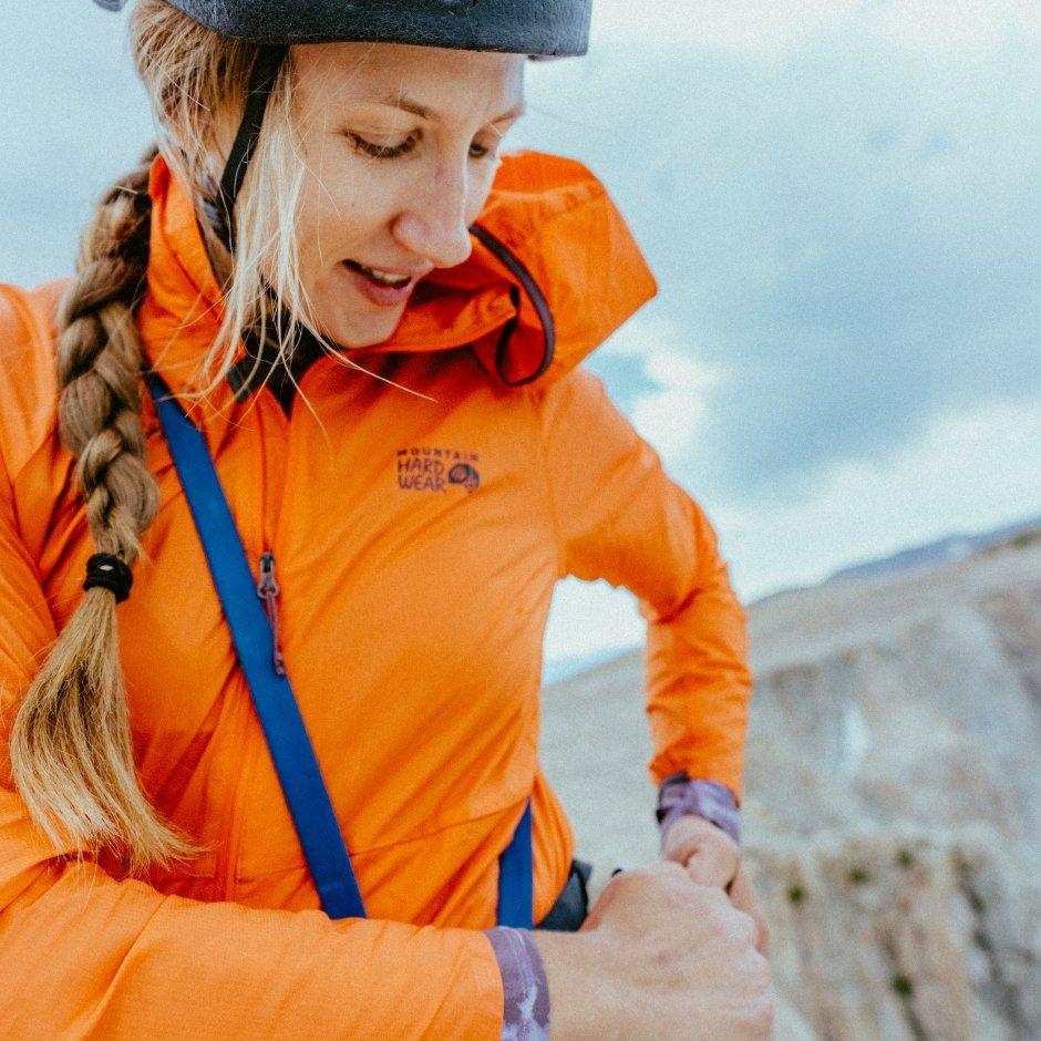 A woman wearing a Kor AirShell™ Jacket and climbing helmet with rocky peaks in the background.



