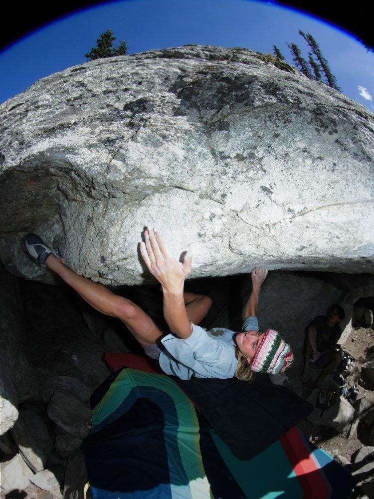 Looking down at a woman with chalky hands, bouldering in a relaxed-fit tee above a crash pad.


