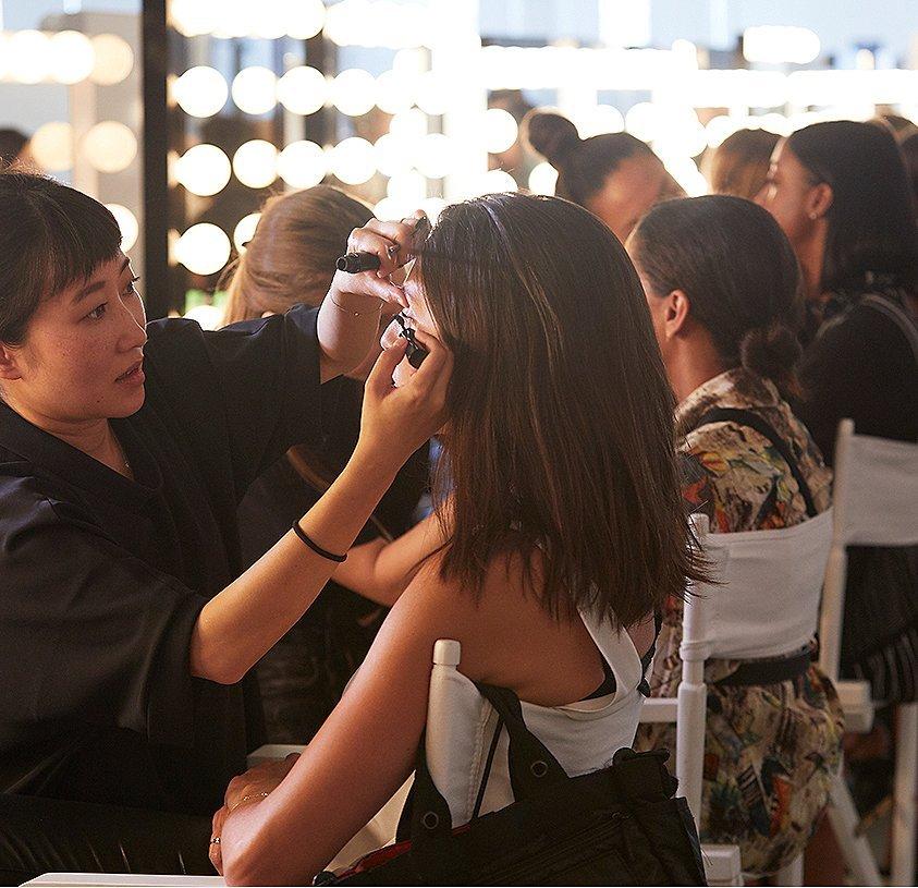 A row of sitting women getting their makeup done
