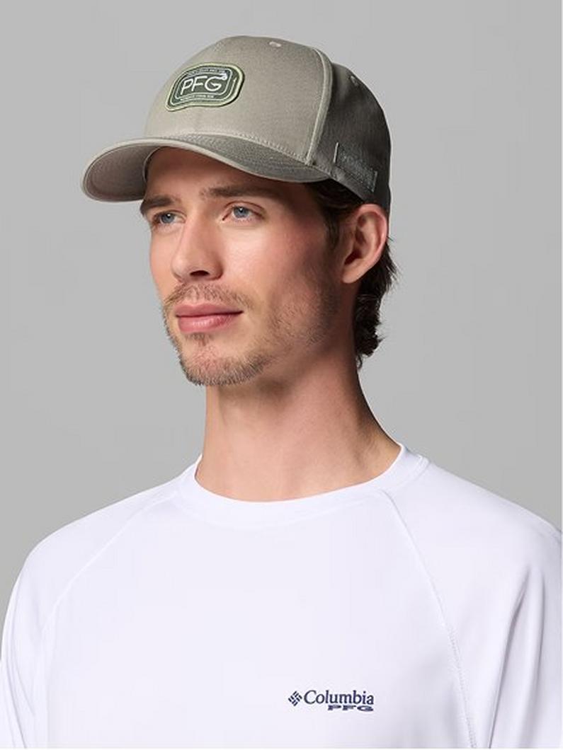 Man wearing a tan and black mesh trucker hat with logo patch and white long-sleeve shirt.