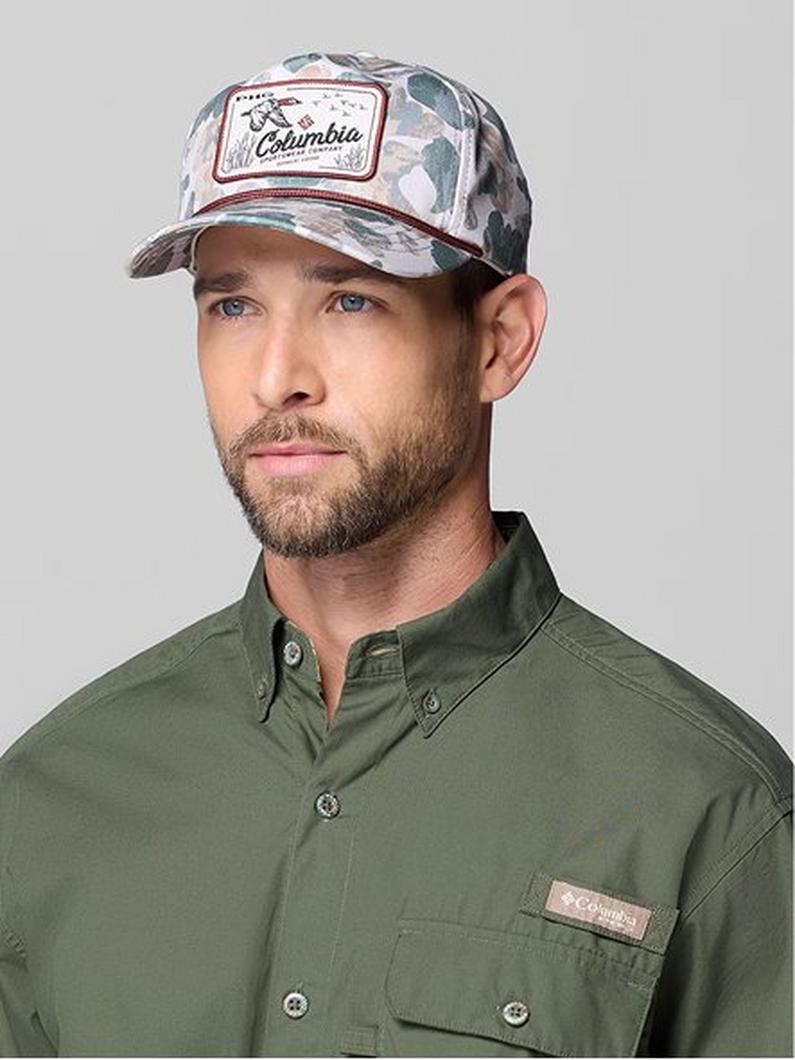 Man wearing camouflage trucker cap with patch and olive green button-up shirt.