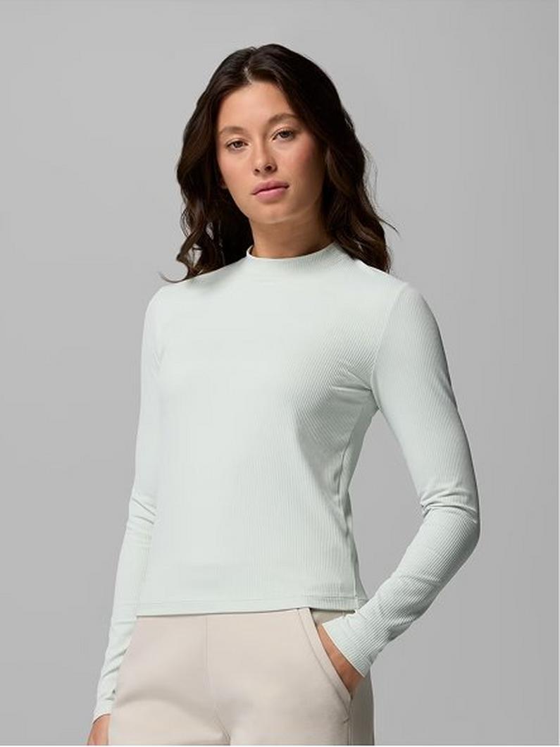 Woman wearing a mint green ribbed long-sleeve top with mock neck and beige pants.