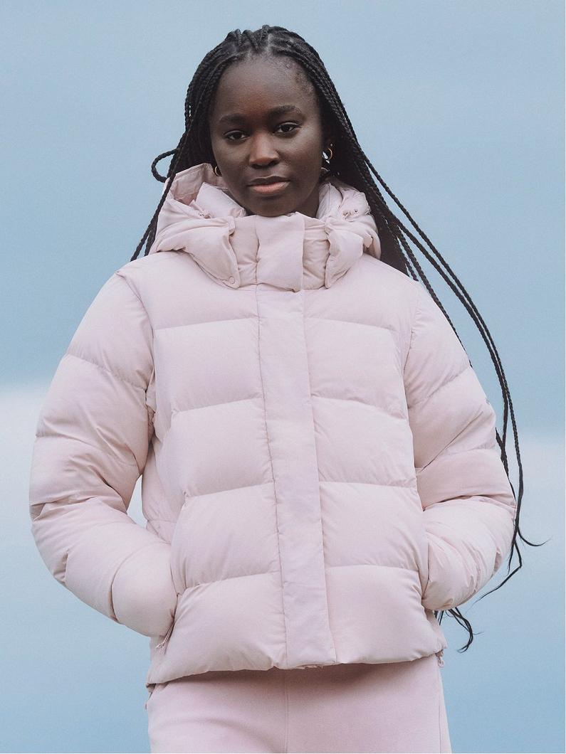 Model wearing a light pink quilted puffer jacket with high collar and hands in pockets.