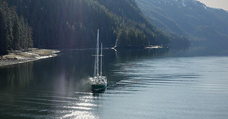 The Emerald ship sailing along a forested coastline. 