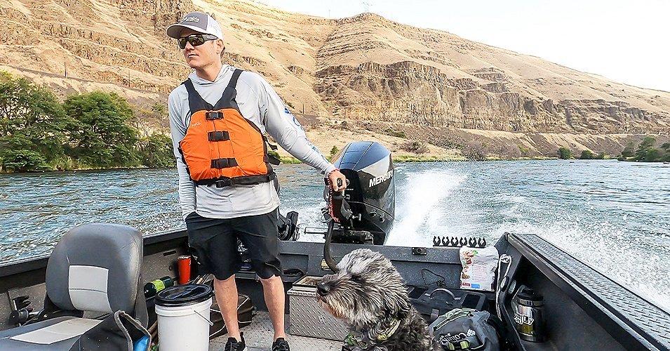 Curits Ciszek and a dog are riding on a boat out on the water.