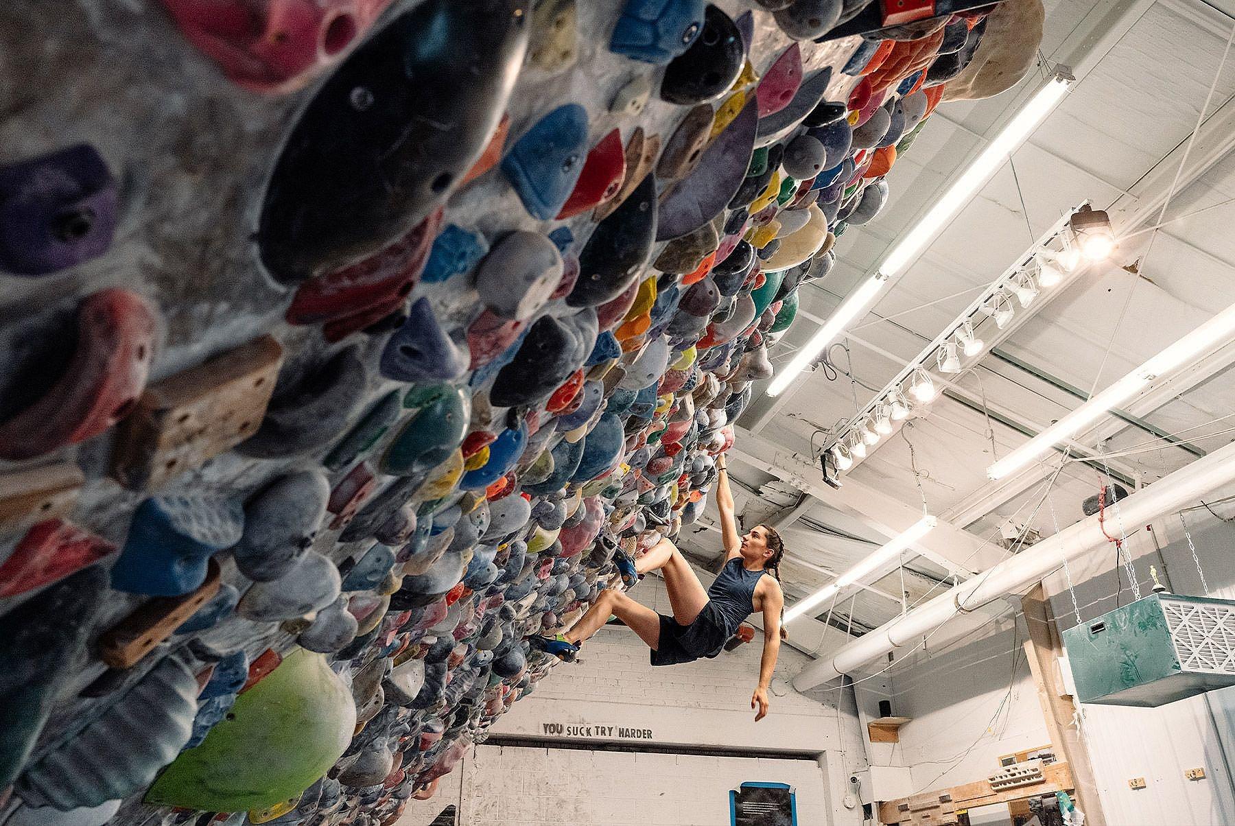 Kyra on a bouldering problem, with her mantra "you suck try harder" in the background 