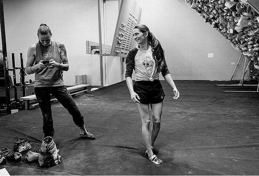 Black and white image of Alex and Kyra standing and talking in the gym