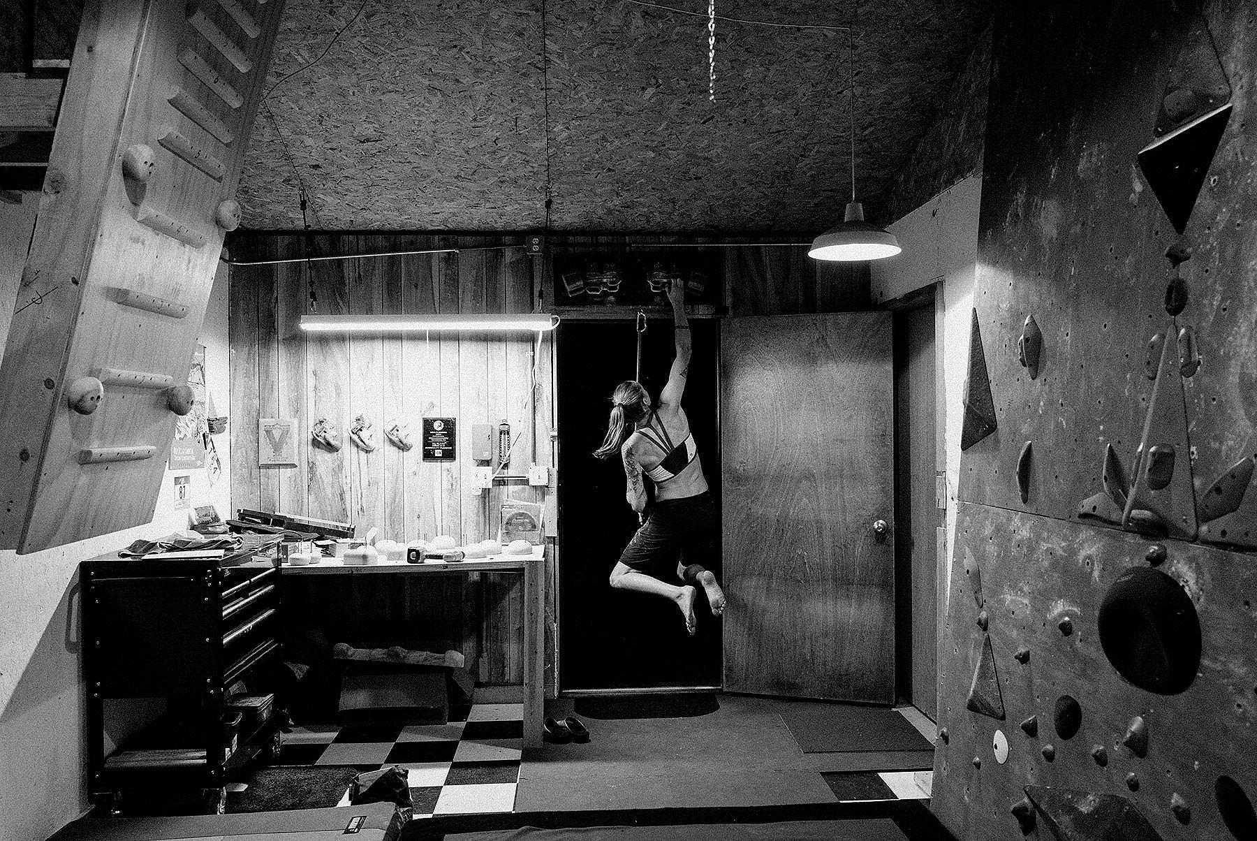 Black and white image of Alex doing hangboard exercises in her home gym