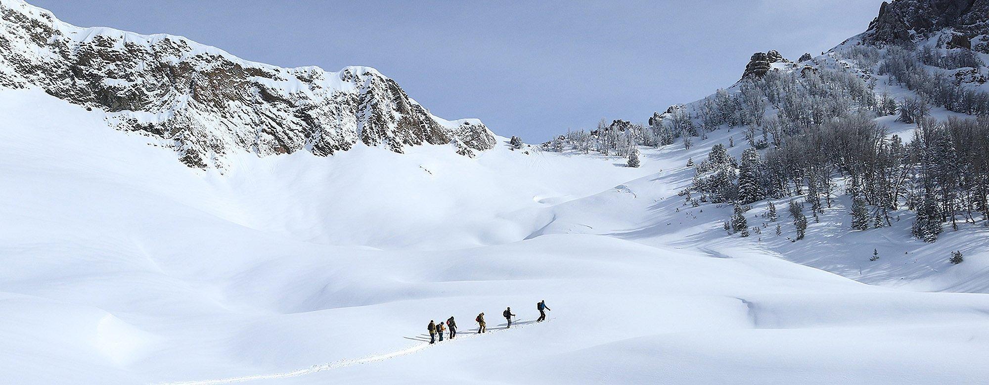 Skiers in the distance skinning up a mountain in the backcountry.  