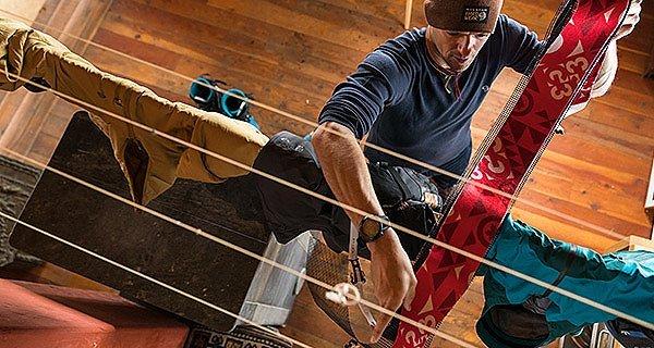 Mountain Hardwear athlete Luke Smithwick taking skins of a drying rack in a ski hut off grid.