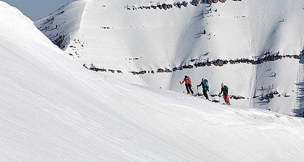 Three skiers in the distance doing a hike-to in a ski resort.