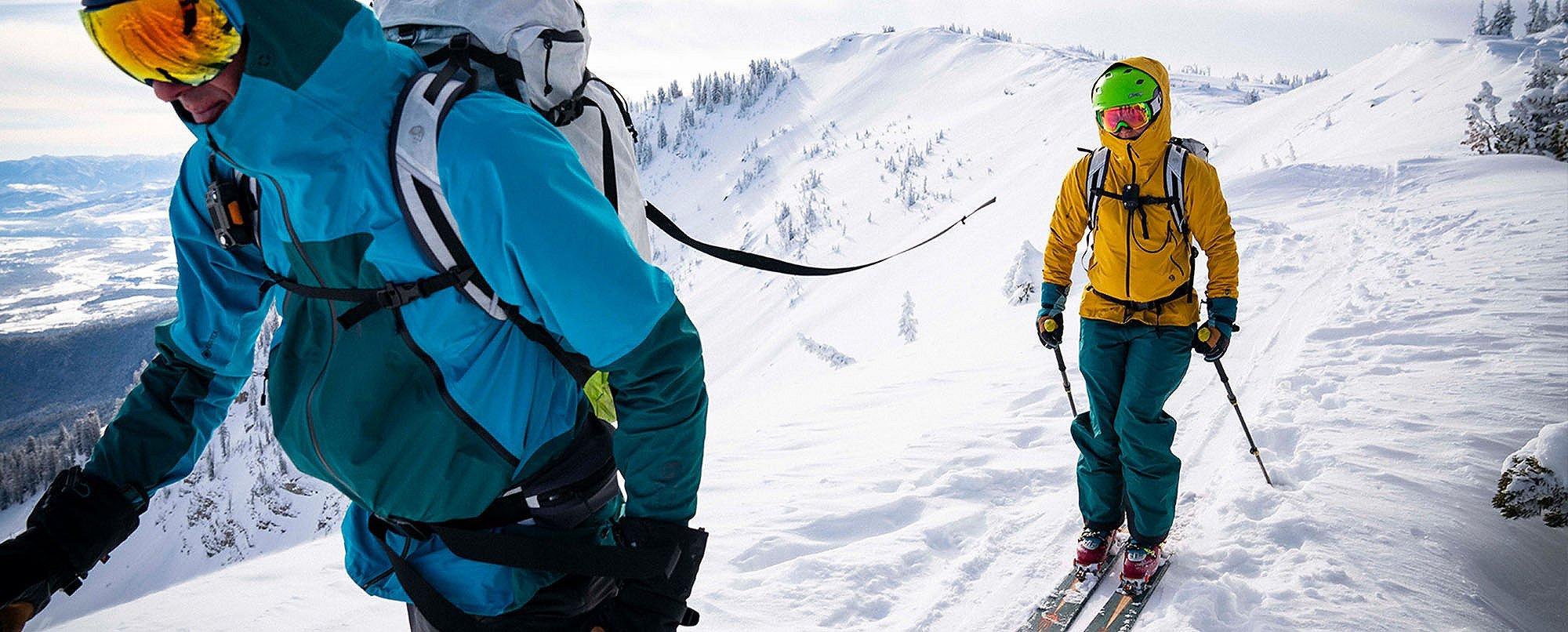 Skiers in the distance skinning up a mountain in the backcountry wearing the Men's High Exposure™ Gore-Tex® C-Knit™ Jacket and Women's High Exposure™ Gore-Tex® C-Knit™ Anorak. 